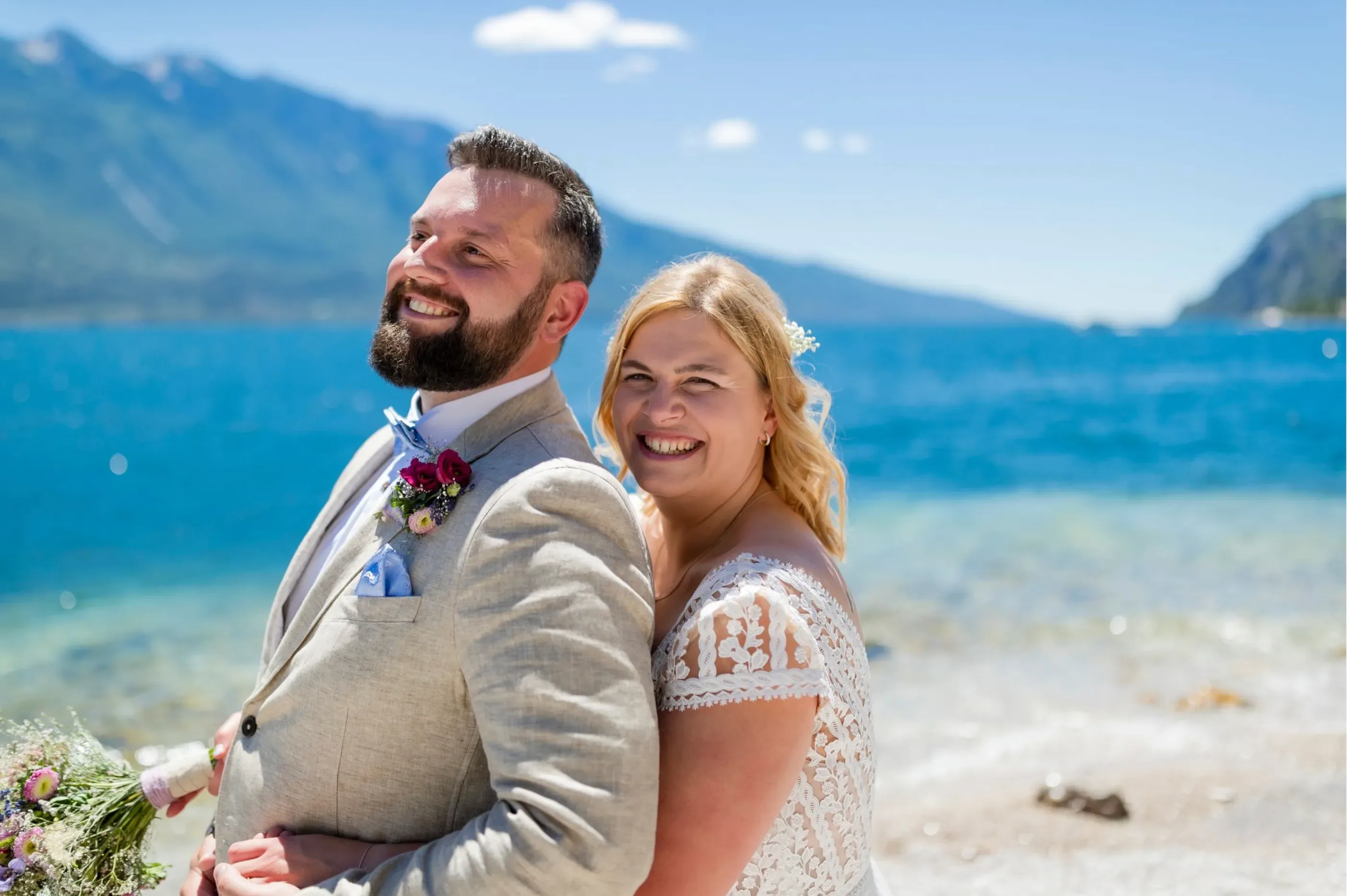 Lächelndes Hochzeitspaar posiert am Strand vor Meereskulisse